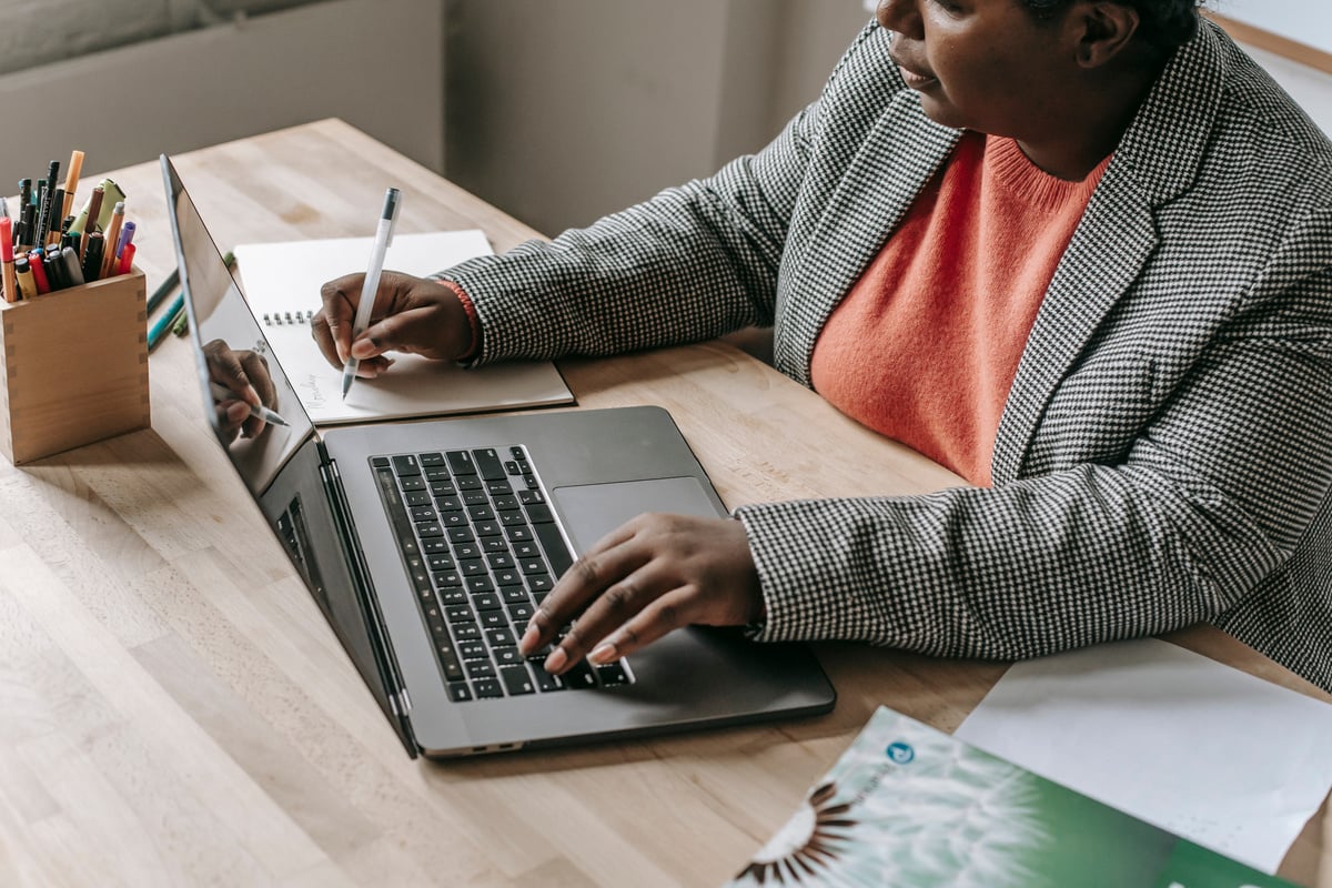 Black woman typing on laptop and writing